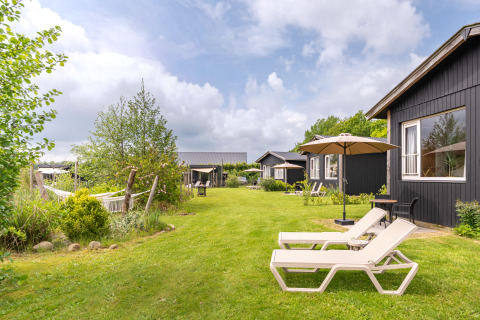 Green lawn with loungers, umbrellas, and black tiny houses at De Kremmer, Netherlands, on a sunny day.