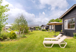 Groen gazon met ligstoelen, parasols en zwarte tiny houses bij De Kremmer, Nederland, op een zonnige dag.