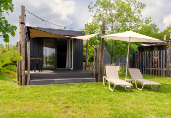 Tiny House bei De Kremmer in den Niederlanden mit Terrasse, Liegestühlen und Gartenschirmen im Grünen.