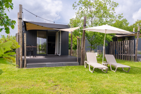 Tiny House at De Kremmer in the Netherlands with a deck, lounge chairs, umbrellas, and a lush green yard.