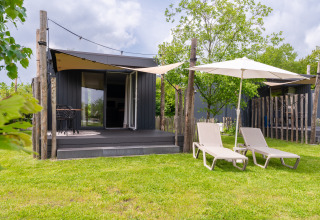 Tiny House at De Kremmer in the Netherlands with a deck, lounge chairs, umbrellas, and a lush green yard.
