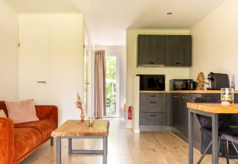 Kompaktes Wohnzimmer und Küche im Tiny House at De Kremmer, Niederlande, mit orangefarbenem Sofa.
