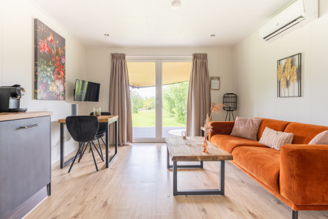 Bright living area in Tiny House at De Kremmer, Netherlands, featuring an orange sofa and garden view.