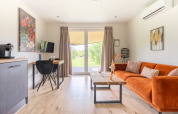 Helles Wohnzimmer im Tiny House at De Kremmer, Niederlande, mit orangefarbenem Sofa und Gartenausblick.