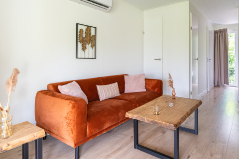 Modern living room in Tiny House at De Kremmer, Netherlands with orange couch, wood tables, and decor.