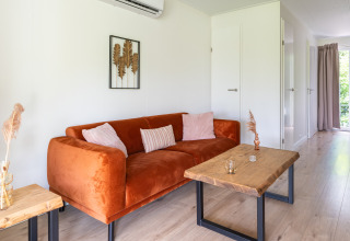 Modern living room in Tiny House at De Kremmer, Netherlands with orange couch, wood tables, and decor.