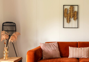 Hébergement glamping cosy avec canapé orange, coussins déco, œuvre murale et éléments naturels.