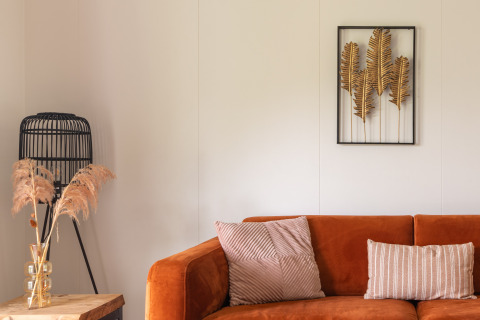 Gemütliche Glamping-Unterkunft mit orangefarbenem Sofa, Zierkissen, Wandkunst und Naturdeko.