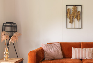 Cozy glamping accommodation with an orange sofa, decorative pillows, wall art, and natural decor elements.