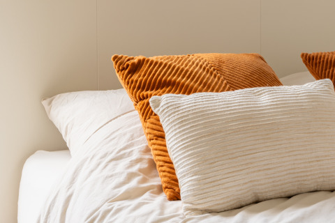 Nahaufnahme eines gemütlichen Betts in einer Glamping-Unterkunft mit weißen und orangen Kissen und Decke.