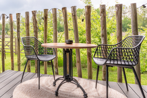 Two black chairs and a round table on a deck at Tiny House at De Kremmer, Netherlands, with a rustic fence.