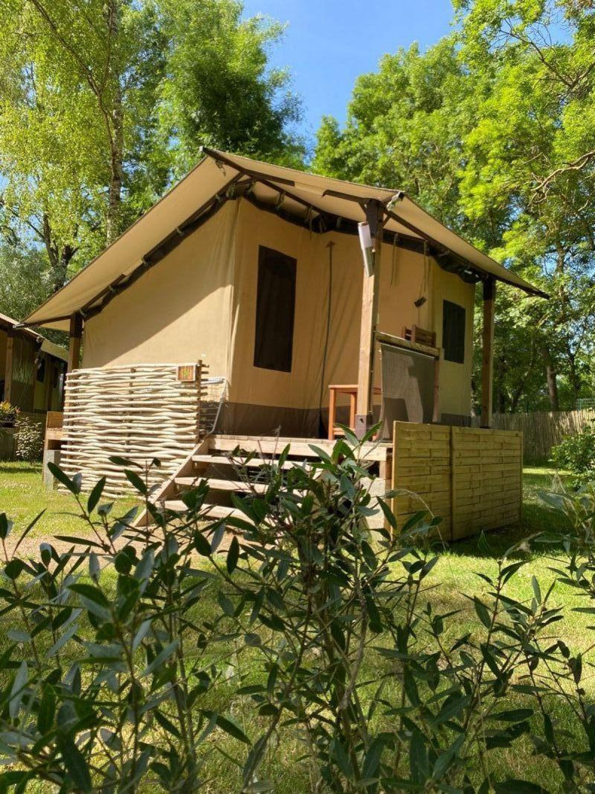 Safaritent Lodge Balearic bij Camping les Rives de Grand Lieu in Frankrijk, omgeven door groene bomen.