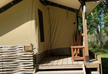 Tenda safari Lodge Balearic al Camping les Rives de Grand Lieu in Francia, con veranda in legno e sedia.