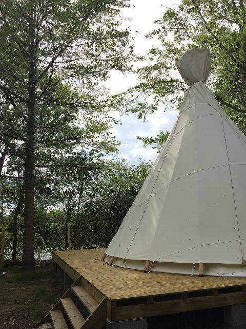 Grande tenda tipi su pedana in legno circondata da alberi al Camping les Rives de Grand Lieu in Francia.