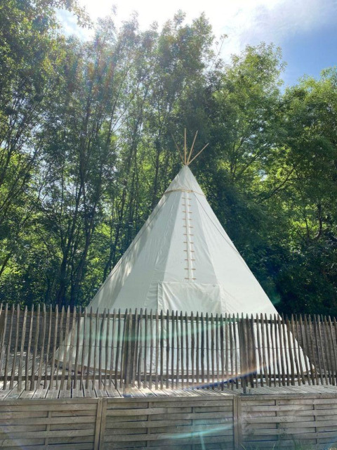 Una tenda tipi bianca al Camping les Rives de Grand Lieu in Francia, circondata da alberi e staccionata.