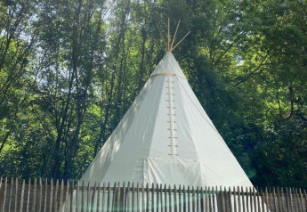 Una tenda tipi bianca al Camping les Rives de Grand Lieu in Francia, circondata da alberi e staccionata.