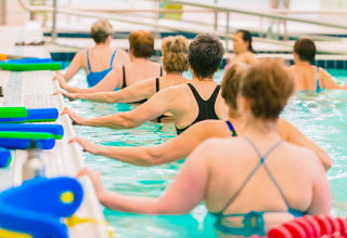 En gruppe voksne deltager i vandaerobic i en indendørs pool på Camping Paradis Le Giessen, Grand Est, Frankrig.