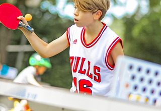 Un ragazzo con maglia dei Bulls gioca a ping pong al Camping Paradis Le Giessen, Grand Est, Francia.