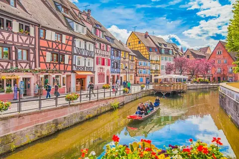 Case a graticcio colorate lungo un canale con fiori a Bassemberg, Grand Est, Francia, persone in barca.