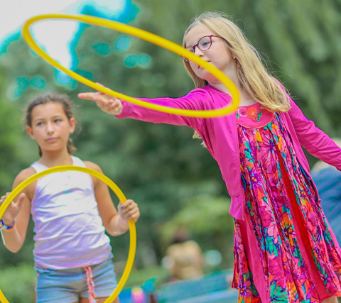 Dos niñas juegan con aros amarillos en el parque de vacaciones Camping Paradis Le Giessen en Grand Est, Francia.