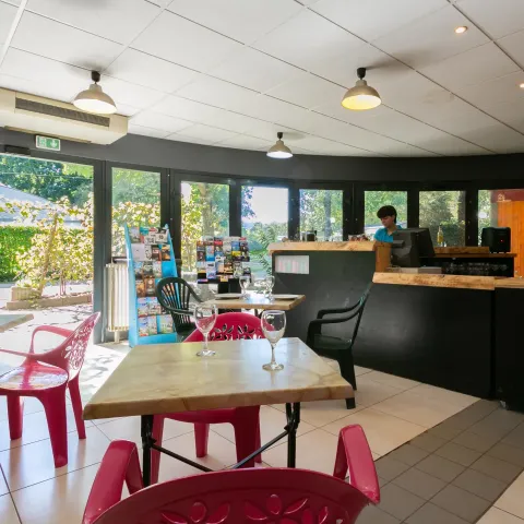 Cafetería luminosa en Camping Paradis Le Giessen, Grand Est, Francia, con sillas de colores y copas en las mesas.
