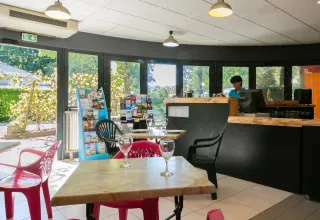 Lichte cafetaria op Camping Paradis Le Giessen in Grand Est, Frankrijk, met kleurrijke stoelen en glazen.