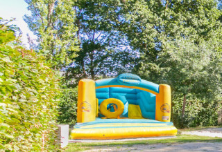 Castillo hinchable en Camping Paradis Le Giessen, rodeado de naturaleza y árboles en Grand Est, Francia.