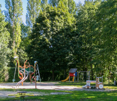 Legeplads omgivet af grønne træer i Camping Paradis Le Giessen, Grand Est, Frankrig, badet i sollys.