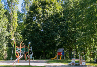 Área de juegos entre árboles en Camping Paradis Le Giessen, Grand Est, Francia, en un día soleado.
