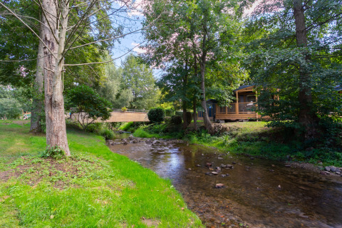 Parco vacanze tranquillo con ruscello, alberi verdi e chalet in legno al Camping Paradis Le Giessen, Grand Est, Francia.