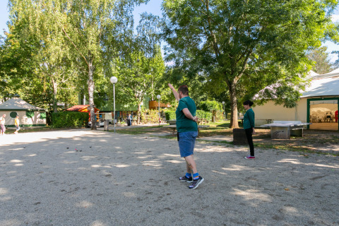 Personas jugando petanca en un camping rodeado de árboles en Camping Paradis Le Giessen, Grand Est, Francia.