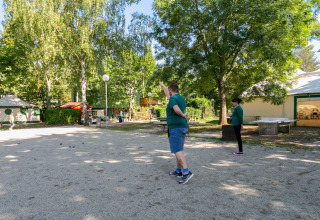 Folk spiller petanque på en campingplads med træer og telte, Camping Paradis Le Giessen i Grand Est, Frankrig.