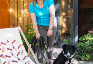 Mujer con camiseta azul y perro blanco y negro afuera en Camping Paradis Le Giessen, Grand Est, Francia.