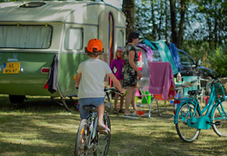 Bambino in bici vicino a una roulotte con famiglia al parco vacanze in Grand Est, Francia.