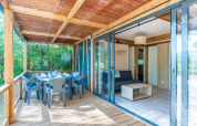 Terraza de madera y sala de una Cottage Premium 3 en Camping Paradis Le Giessen, rodeada de árboles en Francia.