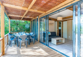 Terraza de madera y sala de una Cottage Premium 3 en Camping Paradis Le Giessen, rodeada de árboles en Francia.