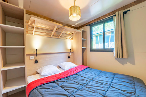 Dormitorio moderno con cama doble, lámparas de pared y ventana en Cottage Premium 3 en Camping Paradis Le Giessen.