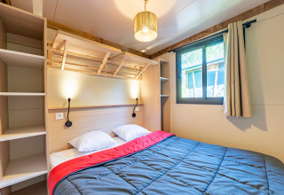 Dormitorio moderno con cama doble, lámparas de pared y ventana en Cottage Premium 3 en Camping Paradis Le Giessen.