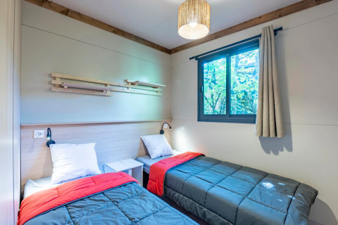 Dormitorio con dos camas individuales, ventana y decoración moderna en Cottage Premium 3 de Camping Paradis Le Giessen, Francia.
