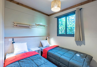 Dormitorio con dos camas individuales, ventana y decoración moderna en Cottage Premium 3 de Camping Paradis Le Giessen, Francia.