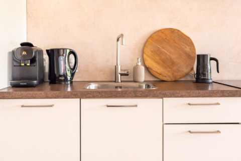 Modern kitchenette in Tiny House XL at De Kremmer, Netherlands, with coffee maker, kettles, and round board.