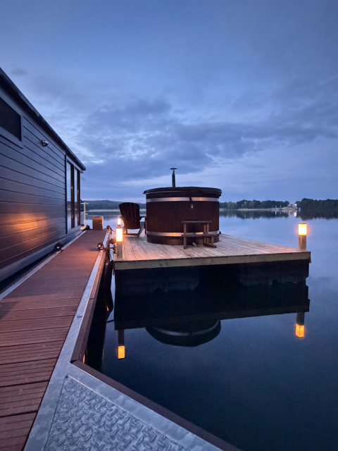 Houseboat ved Marina Mookerplas i Holland med træterrasse, badetønde og aftenbelysning over søen.