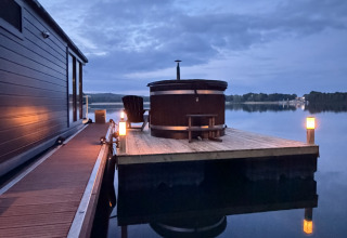 Casa flotante en Marina Mookerplas, Países Bajos, con terraza de madera, jacuzzi y luces al atardecer sobre el lago.