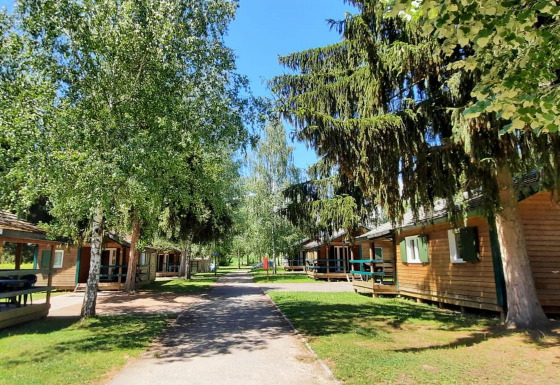 Zonnig uitzicht bij Onlycamp Camping l'Orée d'Alsace met houten chalets, bomen en grasvelden in Frankrijk.