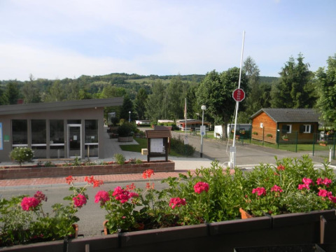 Blick auf den Onlycamp Camping l'Orée d'Alsace in Grand Est, Frankreich, mit Blumenbeeten und Hütten.