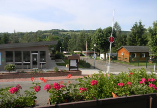 Blick auf den Onlycamp Camping l'Orée d'Alsace in Grand Est, Frankreich, mit Blumenbeeten und Hütten.