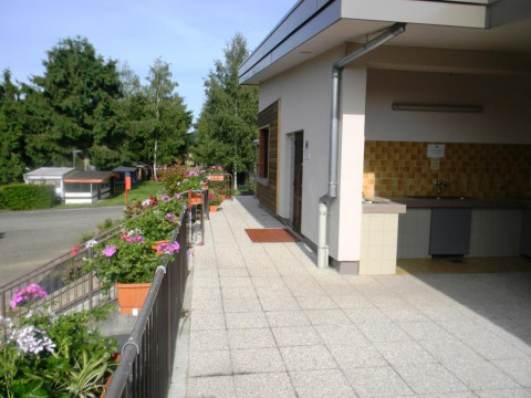 Udsigt over det udendørs køkkenområde og blomsterprydede terrasse på Onlycamp Camping l'Orée d'Alsace.