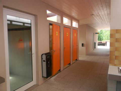 Orangene Toilettenkabinen und Glastür in einem Gang im Onlycamp Camping l'Orée d'Alsace, Grand Est, Frankreich.