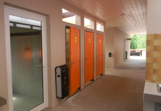 Cabinas de baño naranjas y una puerta de vidrio en el pasillo de Onlycamp Camping l'Orée d'Alsace en Grand Est, Francia.