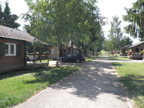 Cabañas de madera y un coche en Onlycamp Camping l'Orée d'Alsace, parque vacacional en Grand Est, Francia.